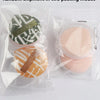 Two packages of soft makeup sponge puffs, one green and one orange, are shown in clear plastic packaging.