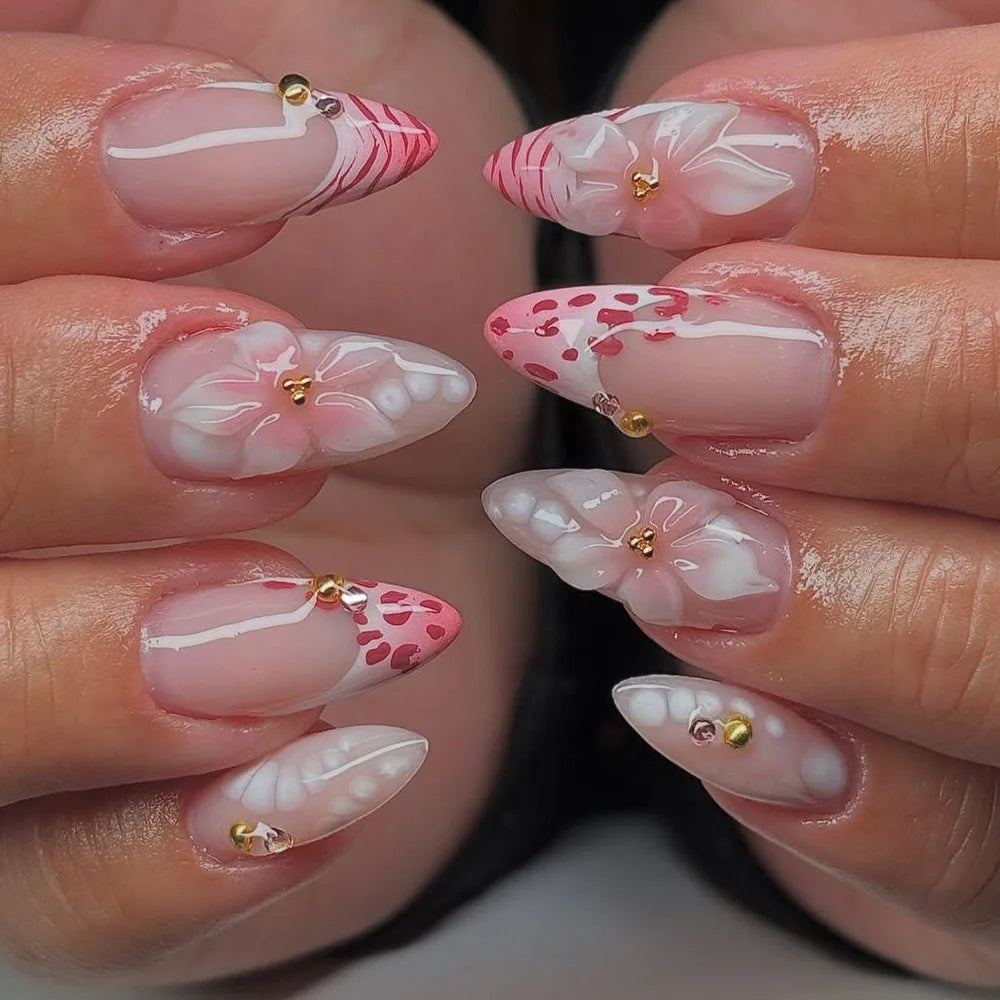 Close-up of fingernails decorated with pink and white floral designs and gold accents.