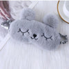 Máscara de ojo de conejo de peluche gris suave con ojos cerrados, descansando sobre una superficie blanca y esponjosa.