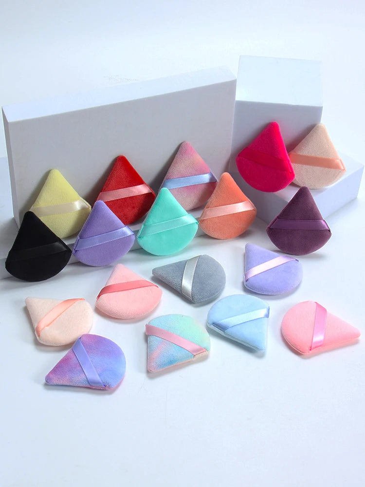 Un set de six éponges de maquillage triangulaires dans diverses teintes de rose, violet, vert et orange, présentées sur une b