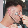 A man is using an all-in-one beard styling template and comb to shape his beard.
