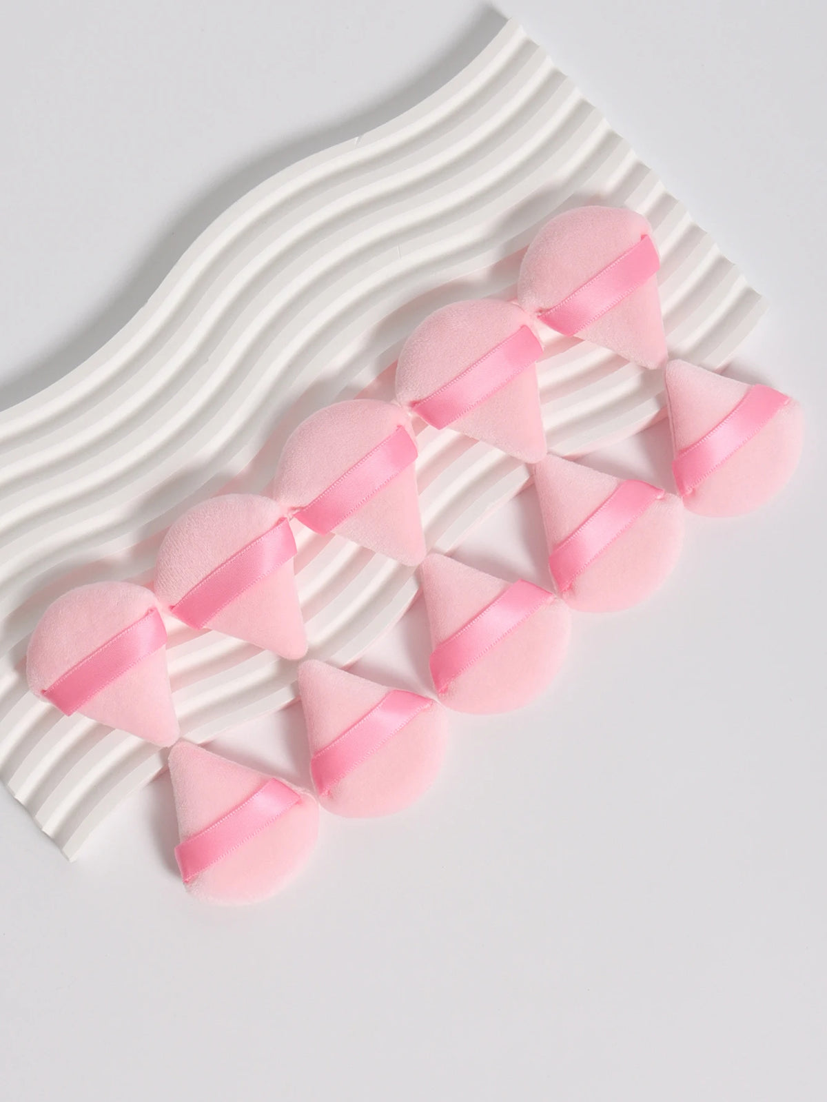 Un ensemble de puffs triangulaires roses disposés en ligne ondulée sur fond blanc.