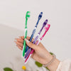 Une main tient plusieurs brosses à dents manuelles colorées, dont des verts, bleues et violettes.