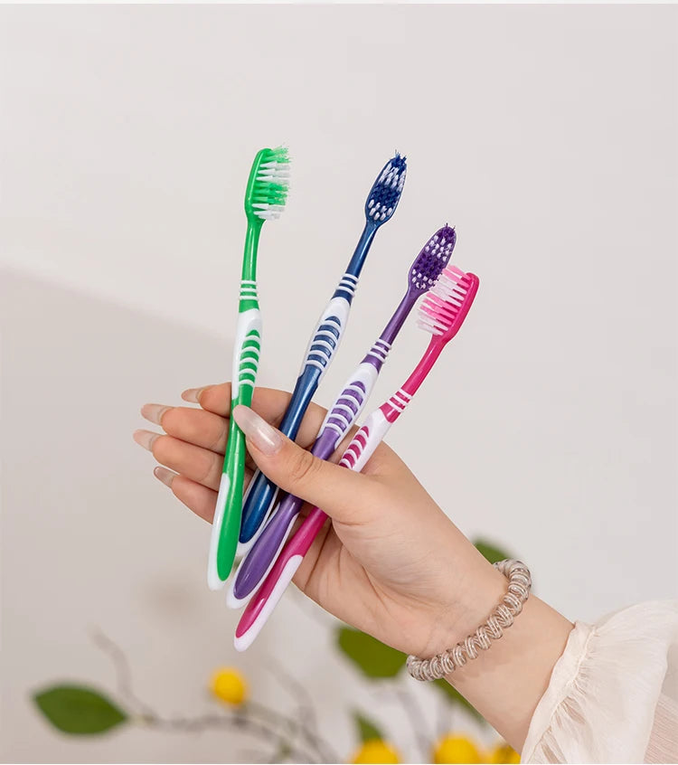 Une main tient plusieurs brosses à dents manuelles colorées, dont des verts, bleues et violettes.