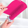 A hand is holding a bright pink silicone heat resistant mat for hair styling tools.