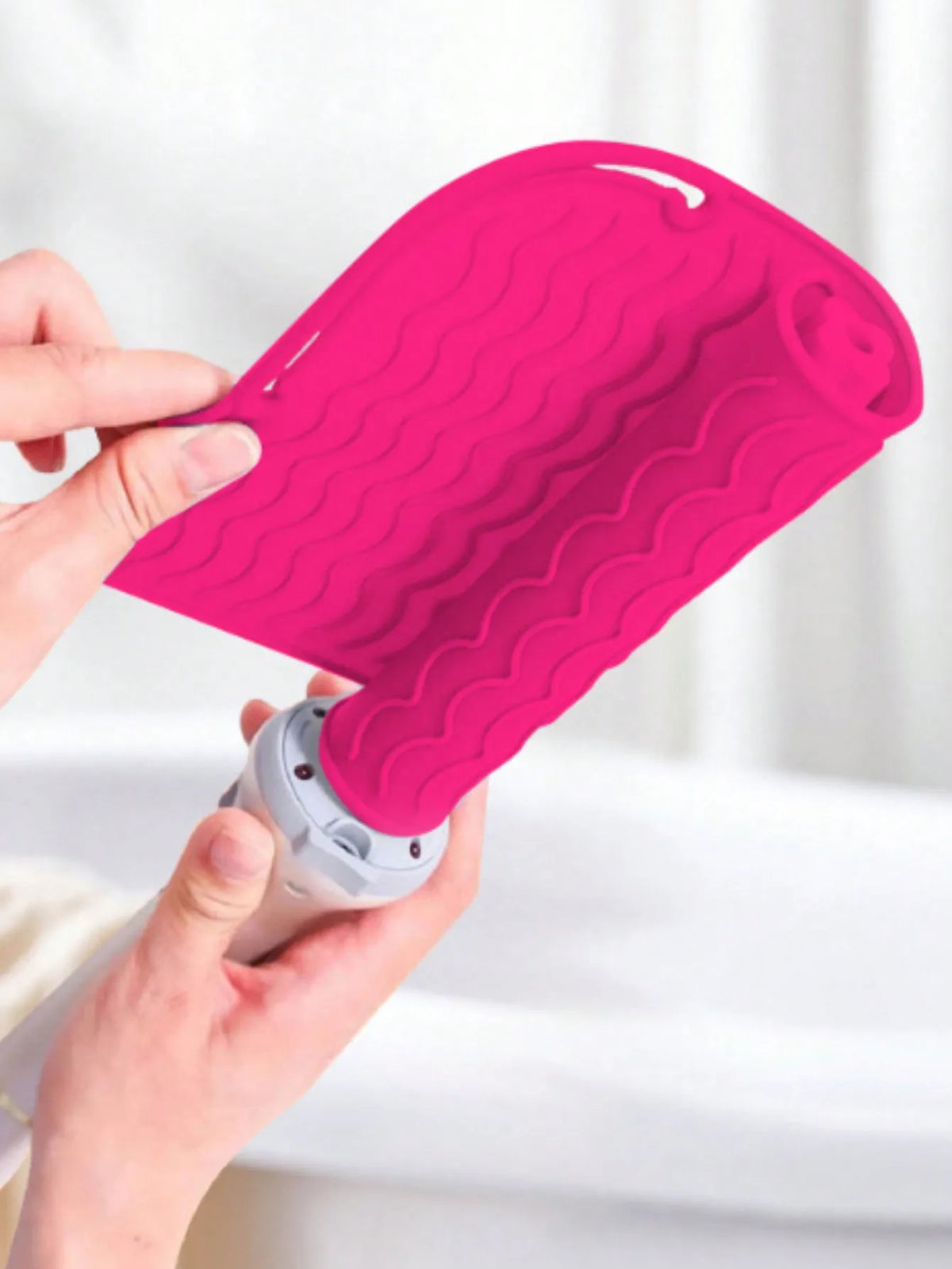 A hand is holding a bright pink silicone heat resistant mat for hair styling tools.