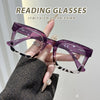 Lila quadratische Lesebrille mit Leopardenmusterrahmen wird von einer Hand gehalten.
