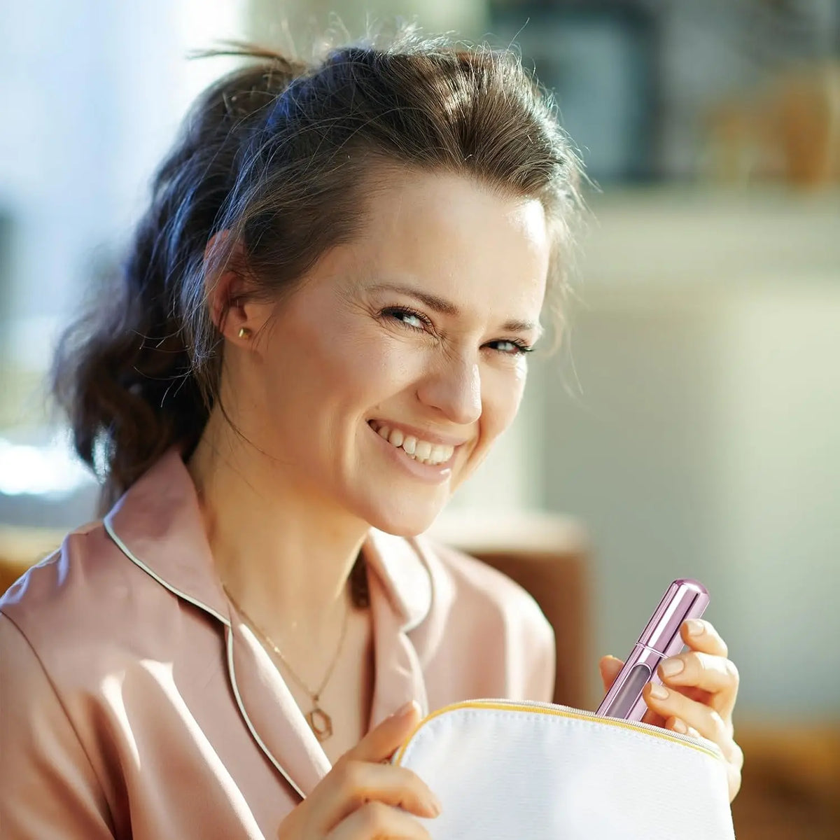Une femme souriante tenant une bouteille de parfum rose rechargeable avec un vaporisateur portable.