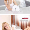 A woman is using a white facial steamer device to treat her face while sitting and steaming.
