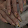 A close-up of a hand displaying 24 press-on nails with a pink flower almond design and gold accents.