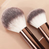 A pair of professional makeup brushes with silver and white bristles and rose gold handles.