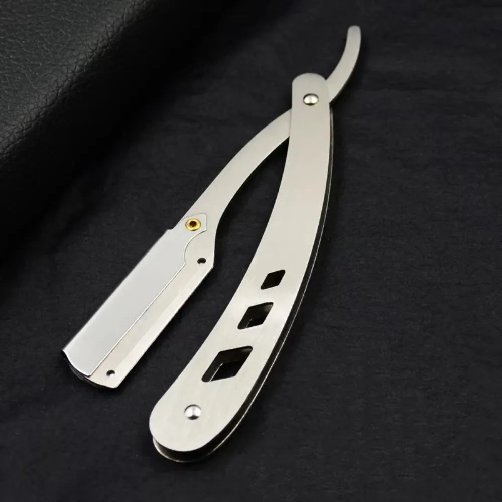 Couteau de rasage antique pliable en argent avec poignée et lame visible sur une surface sombre.