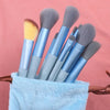 A set of professional makeup brushes with light blue and gray handles resting in a light blue fabric pouch.
