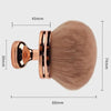 A large, round makeup brush with a gold-toned handle and a fluffy, light beige synthetic hair bristles.