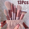 A set of thirteen professional makeup brushes in various shades of pink and nude, displayed on a fluffy white background.