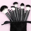 A collection of black and white makeup brushes with sponge tips arranged in a black pouch on a pink background.