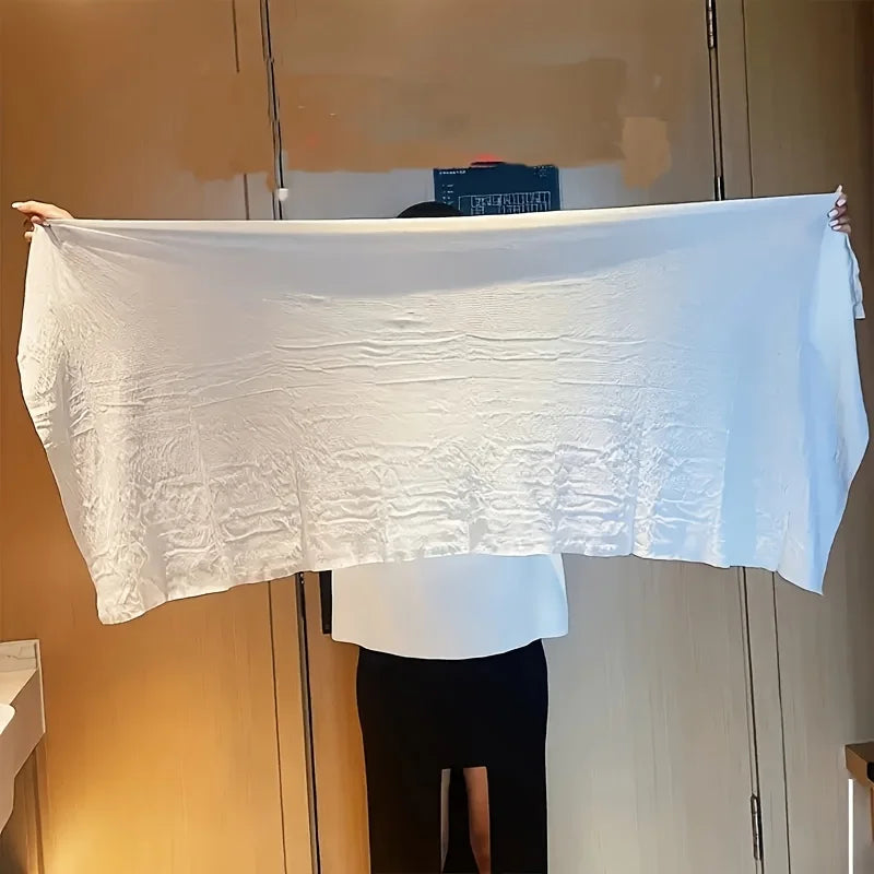 A white extra large disposable towel is displayed flat against a wooden cabinet.