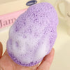 A hand holds a purple exfoliating cleansing sponge used for blackhead removal.
