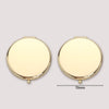 A round, gold-colored portable folding makeup mirror with a magnifying feature.