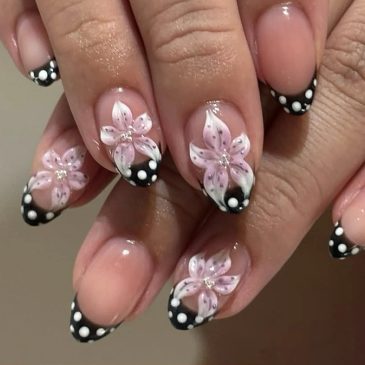 Close-up of a hand displaying pink and black polka dot press-on false nails with an almond shape.