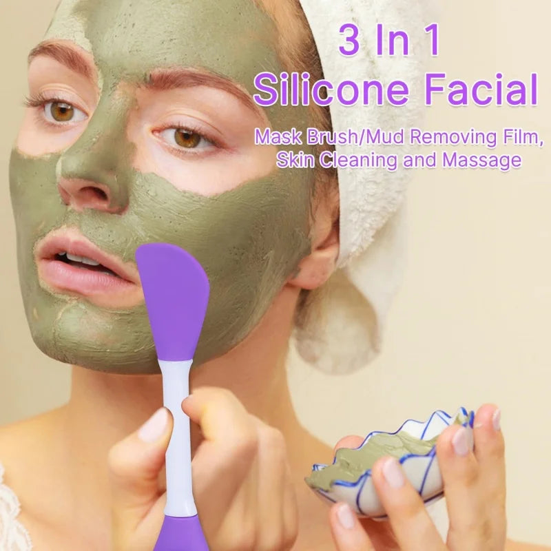 A woman applies a green silicone facial mask using a purple applicator brush on her face.