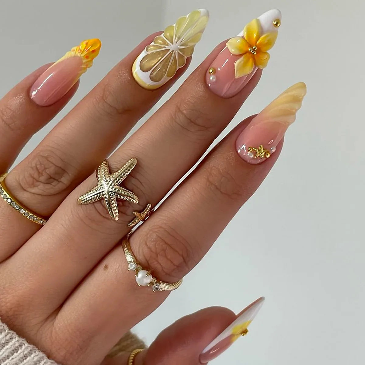 Une main montrant un ensemble d'ongles press-on roses à l'amande française avec des accents floraux et dorés.