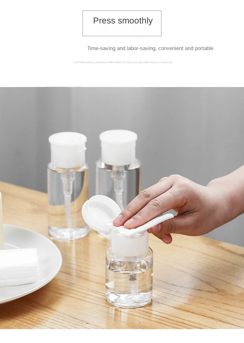 A hand is squeezing a white substance from a clear refillable push-down pump dispenser bottle onto a wooden table.