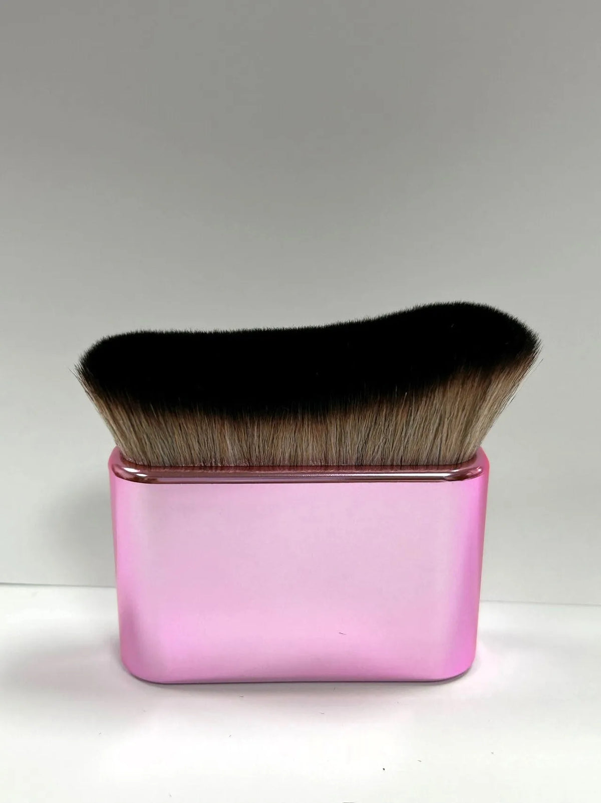 A pink rectangular container holds a black and gold makeup brush for tan and foundation.