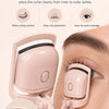 A close-up of a pink electric heated eyelash curler being used on an eye, demonstrating precise lash placement.