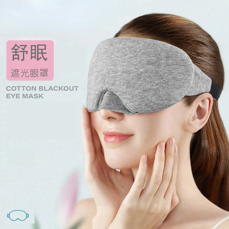 A woman is wearing a gray cotton blackout eye mask while resting her hand on her eye area.