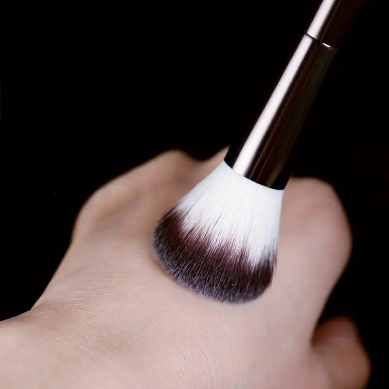 A close-up of a professional double-ended makeup powder brush set with dark brown and white bristles held by a hand against a
