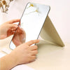 A hand is holding a portable folding makeup mirror, showing a floral design on the reflective surface.