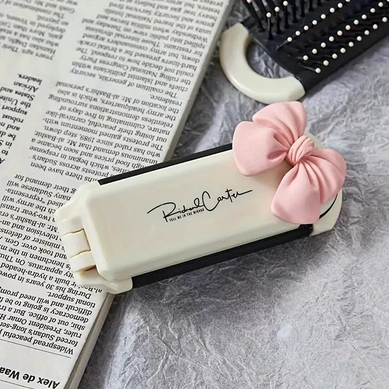 A folding mini hair comb with a mirror for styling, featuring a pink ribbon detail.