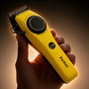 A hand holds a yellow Kemei KM 1735 high-speed motor cordless hair clipper.