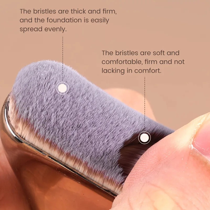 A close-up of a foundation brush with gray nylon bristles being used to apply makeup.