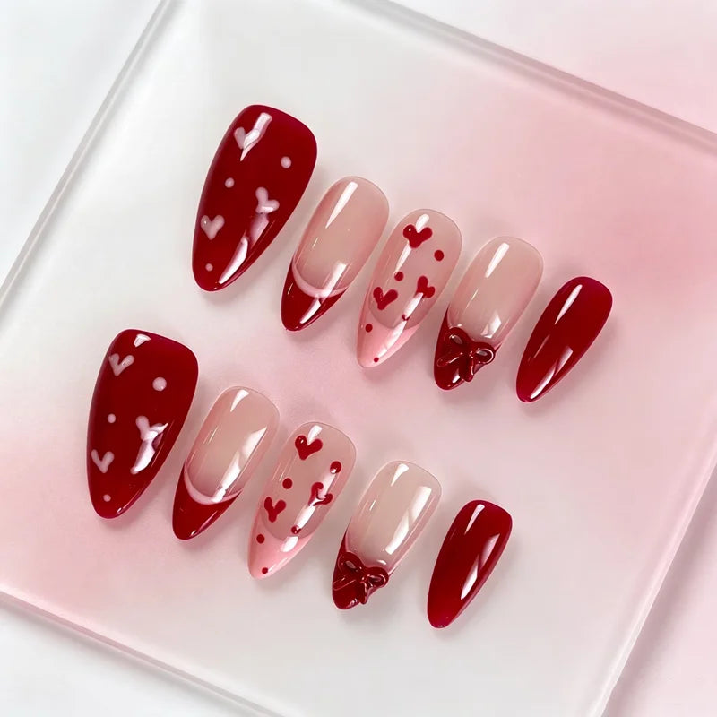 A set of red and pink Y2K almond press-on nails with small heart designs displayed on a clear square plate.