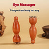 A small, reddish-brown wooden eye massager tool with a rounded top and base, shown against a light background.