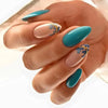 A hand displaying press-on false nails with a teal base and gold floral accents on a natural nail bed.