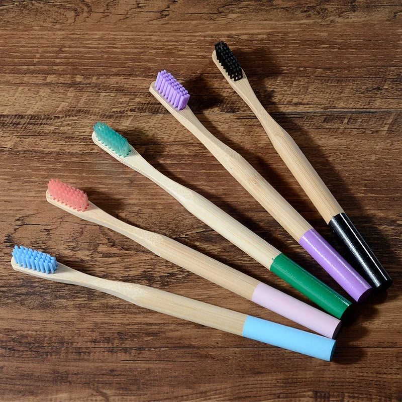 A collection of ten eco-friendly bamboo toothbrushes in various colors, including purple, pink, green, and black bristles.