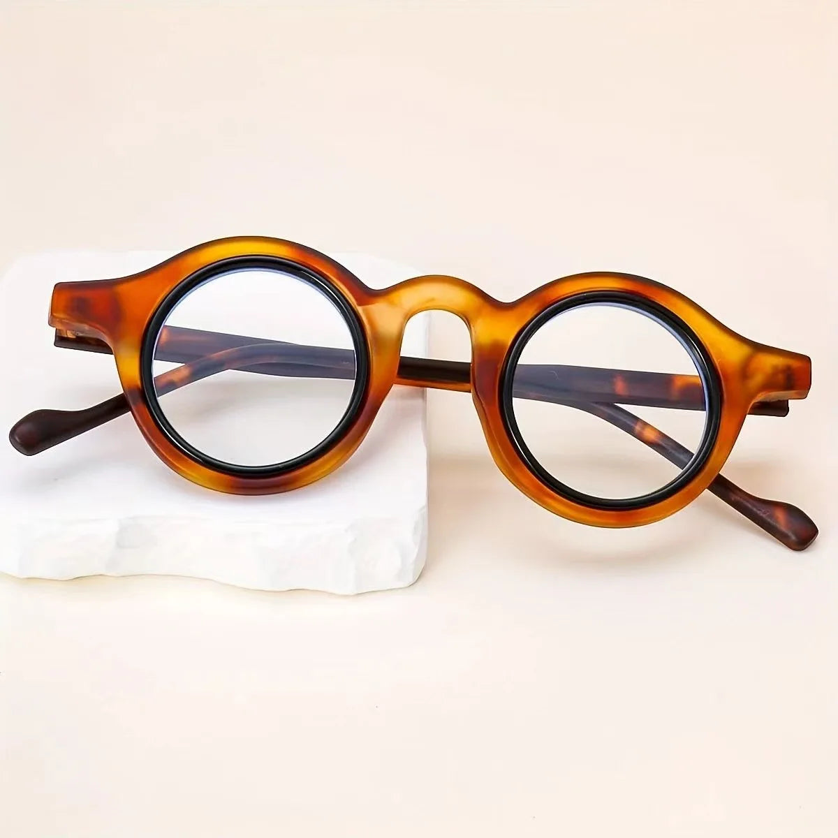 Une paire de lunettes de lecture à monture tortue posée sur une pierre blanche.