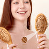 A woman holds a wooden bamboo hair brush with an air hole, demonstrating the product for gentle detangling.