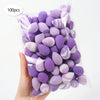 A hand holds a clear plastic bag filled with 100 reusable expandable makeup sponges in purple and white stripes.