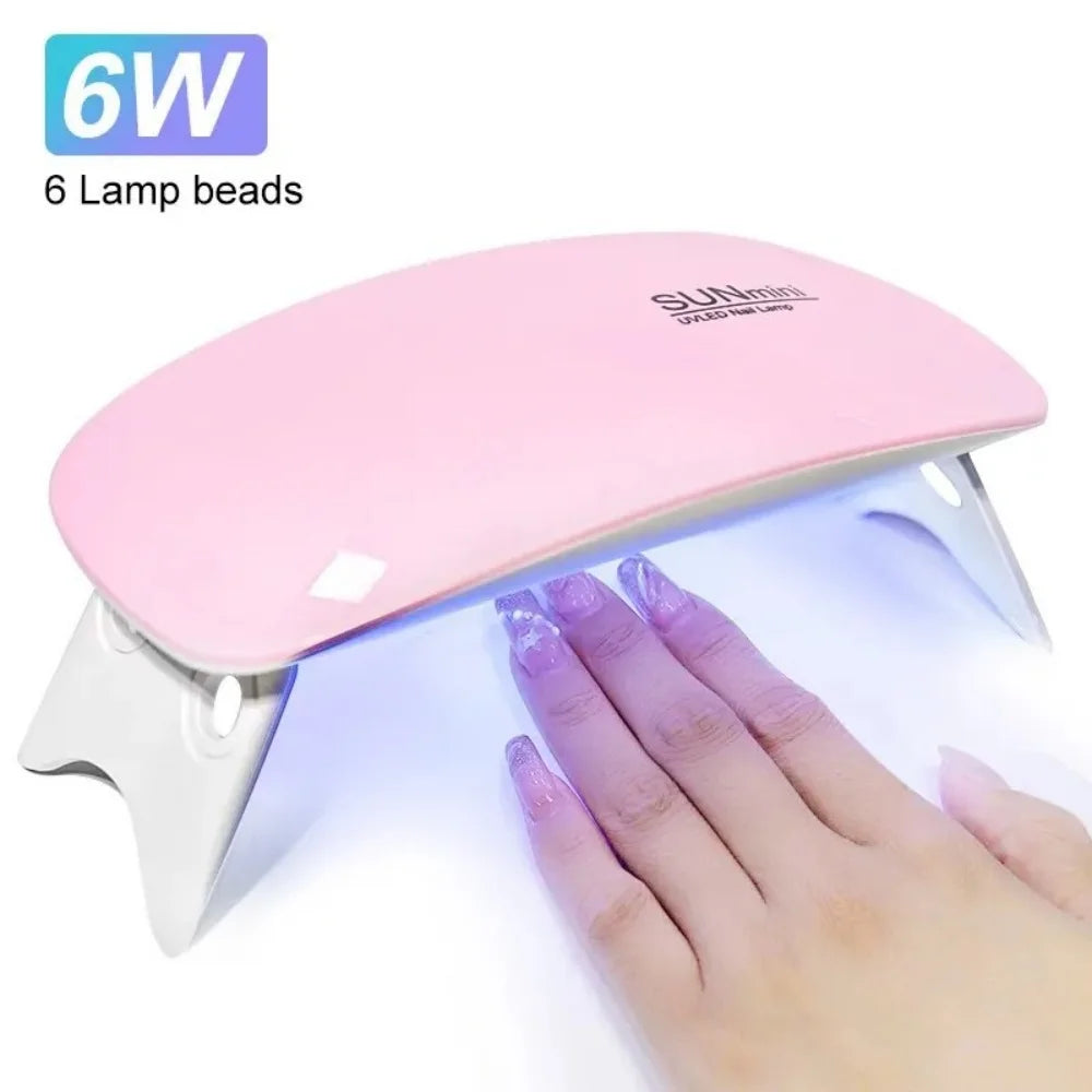 A pink portable UV LED nail dryer lamp with six lamp beads being held by a hand.