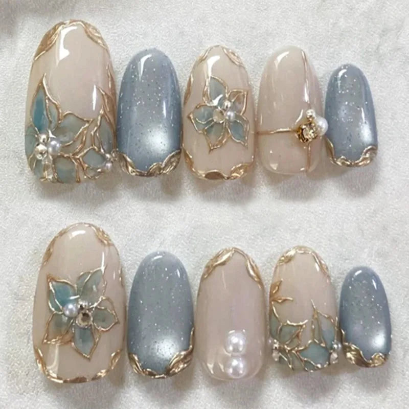 A set of 24 press-on almond nails featuring a pale pink and blue gradient with gold floral and butterfly designs.