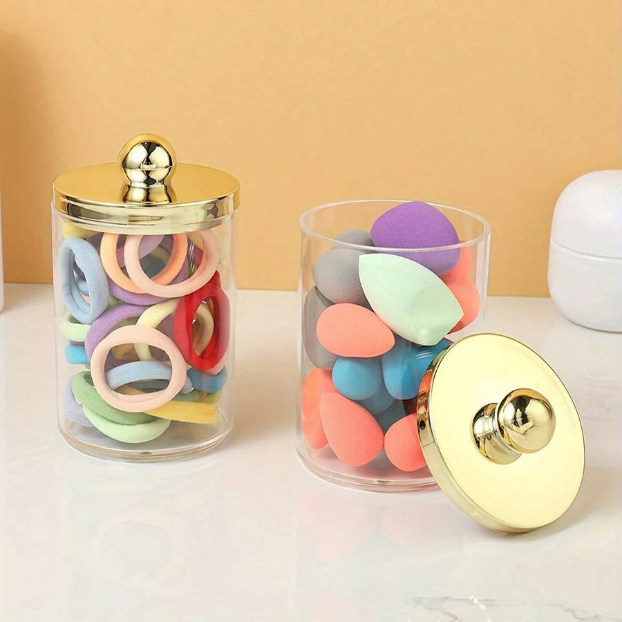 Un distributeur en acrylique transparent contient des anneaux de différentes couleurs et un couvercle doré avec un capuchon a