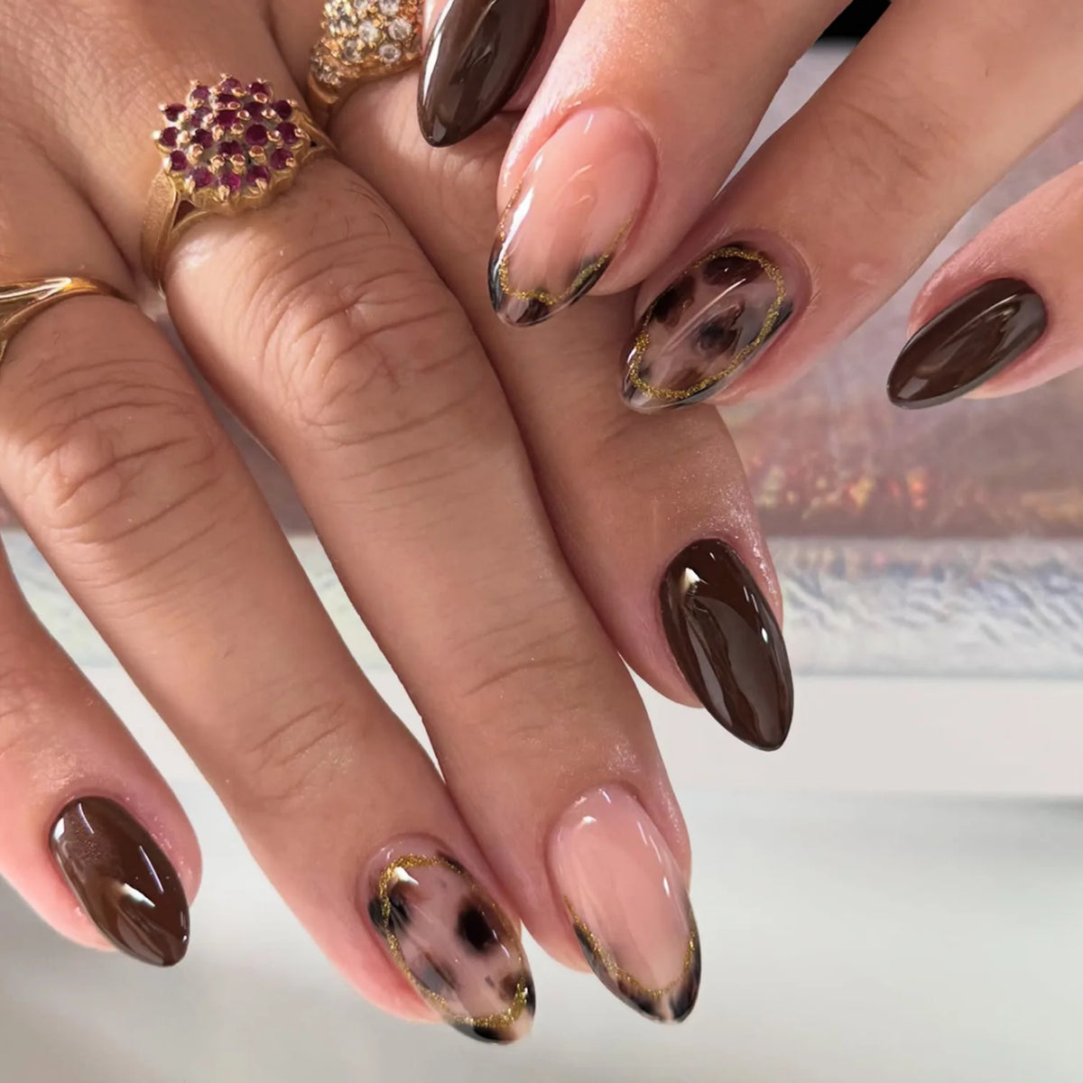 Gros plan sur des mains montrant un ensemble de faux ongles en amande françaises roses avec des accents dorés.