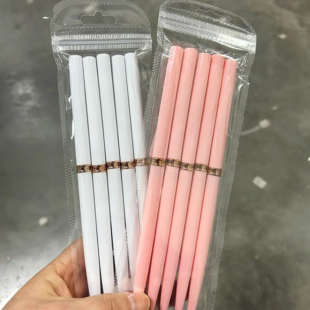 Une main tient un emballage plastique transparent contenant un set de pinceaux pour liner de nail art roses et blancs.