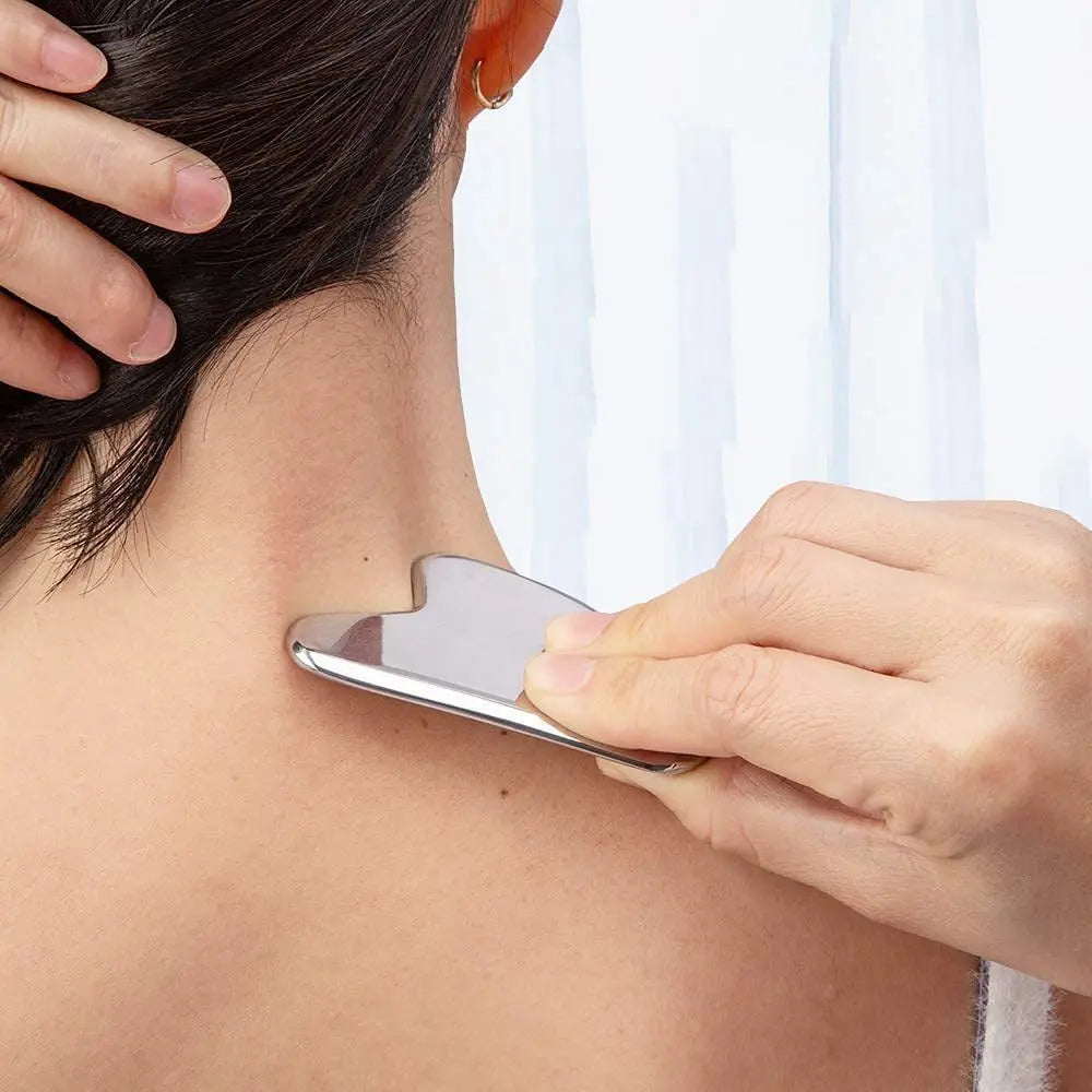 A hand is using a stainless steel gua sha tool on the neck of a person for facial or body massage.