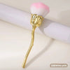 Pincel de maquillaje en forma de rosa dorada con cabeza esponjosa rosa y blanca sobre una superficie blanca.