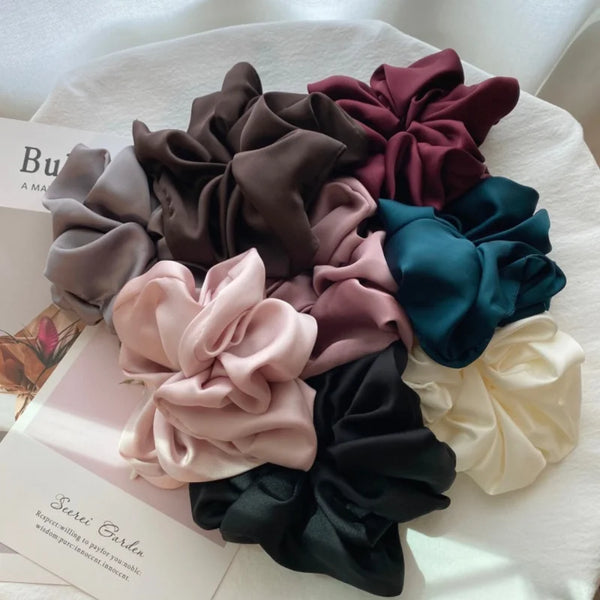 A collection of satin chiffon hair scrunchies in various shades including mauve, dusty rose, deep green, and black.